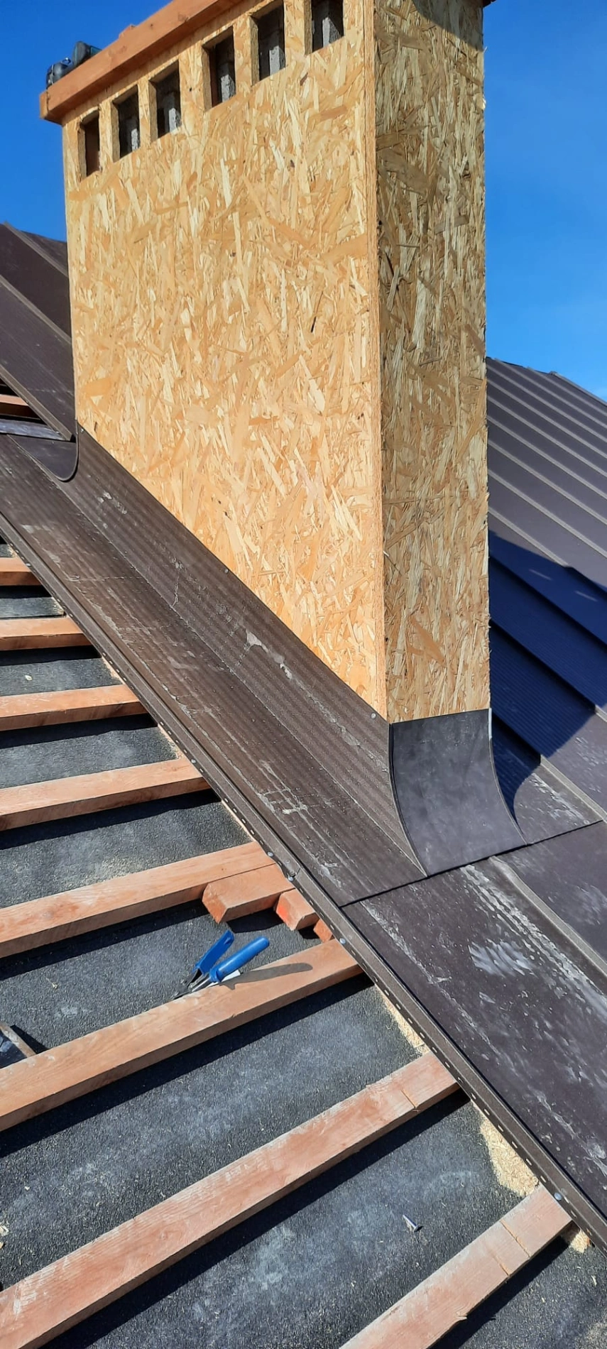 Obróbka komina na dachu, metalowe wykończenie osadzone na podkładzie hydroizolacyjnym i drewnianych łatach pod blachodachówkę