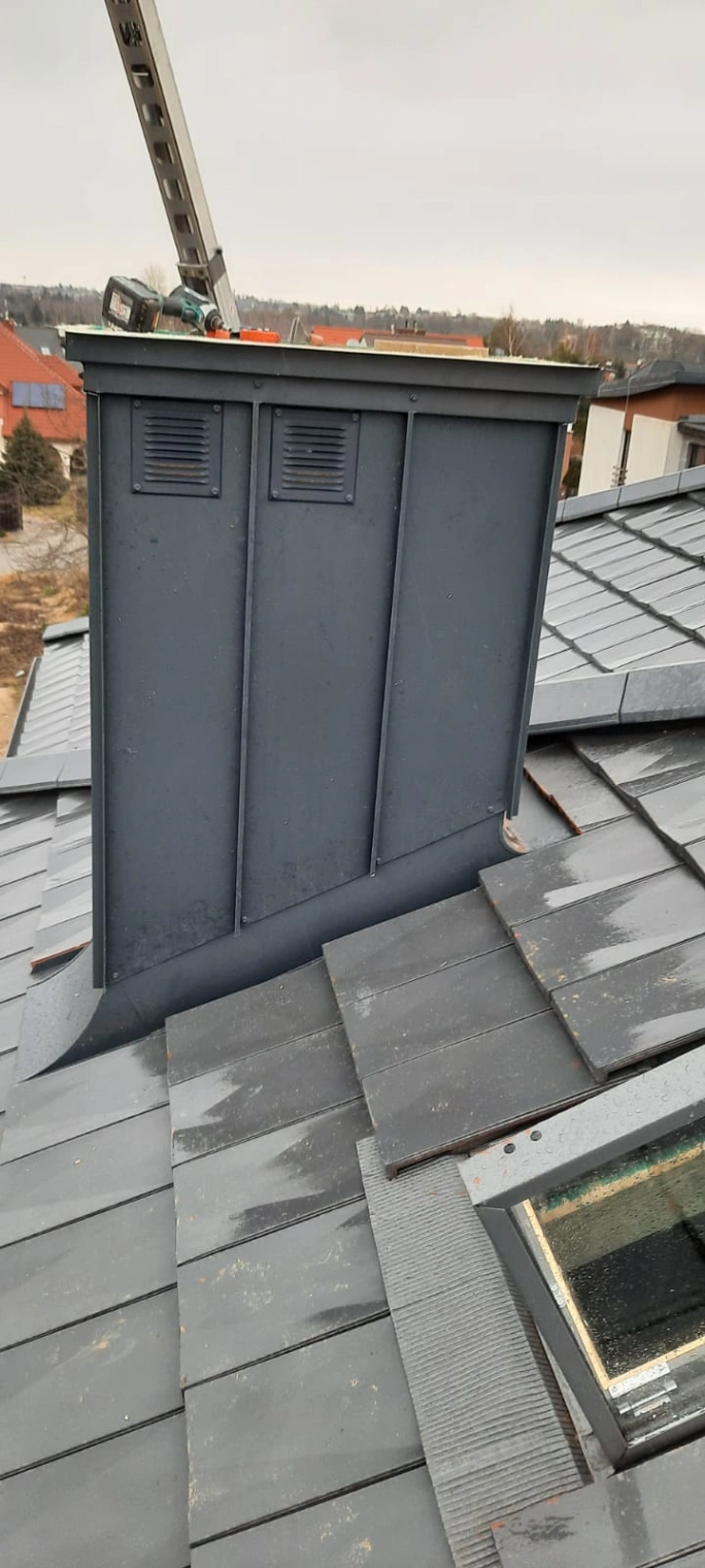 Obróbka komina na dachu pokrytym blachodachówką z widocznym oknem dachowym