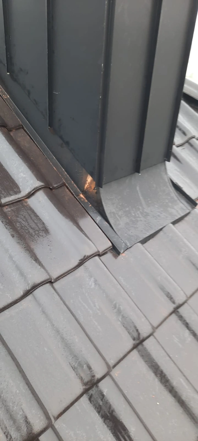 Obróbka komina z metalową obróbką blacharską na ciemnej dachówce betonowej